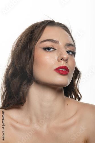 Beauty and make-up concept. Brunette woman with wavy long hair and makeup close-up studio portrait. Model looking with seductive look at camera. Red lipstick and nude makeup. White background