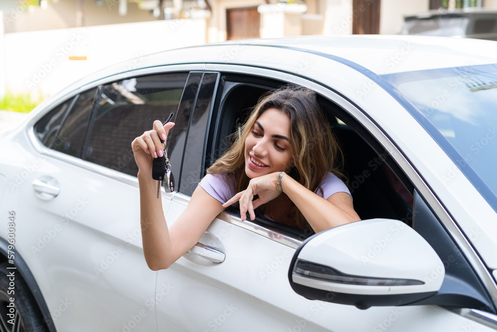Beautiful young happy smiling woman driving her car, showing the keys to a new car