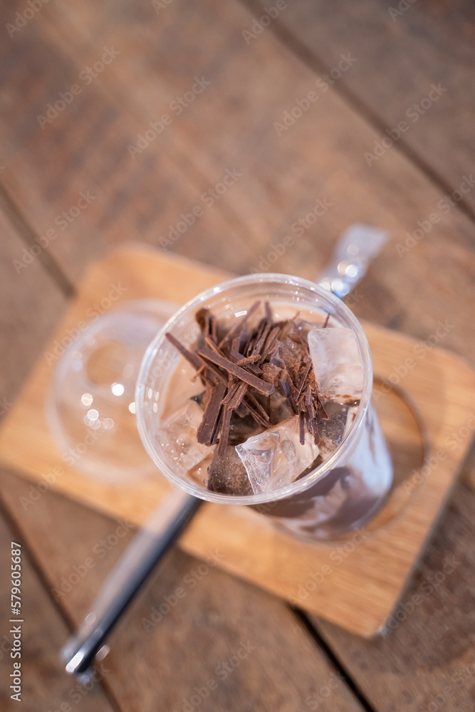 Fototapeta premium Iced chocolate with chocolate chunks on ice in a glass on a wooden coaster