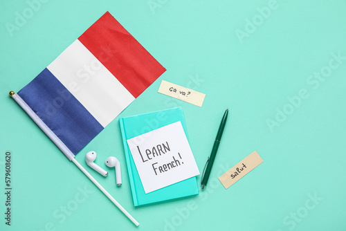 Paper with text LEARN FRENCH, stationery, earphones and flag on green background