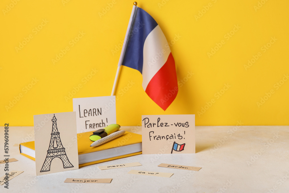 Paper with text LEARN FRENCH, drawn Eiffel Tower, flag and stationery on table near yellow wall - obrazy, fototapety, plakaty 