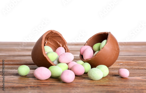 Chocolate Easter egg and candies on wooden table against white background