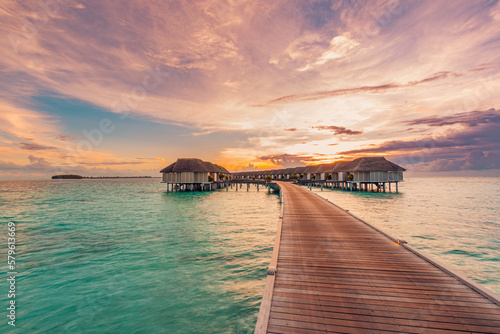 Amazing beach panoramic landscape. Beautiful Maldives sunset seascape view. Horizon colorful sea sky clouds  over water villa pier pathway. Tranquil island lagoon  vacation travel panorama background 