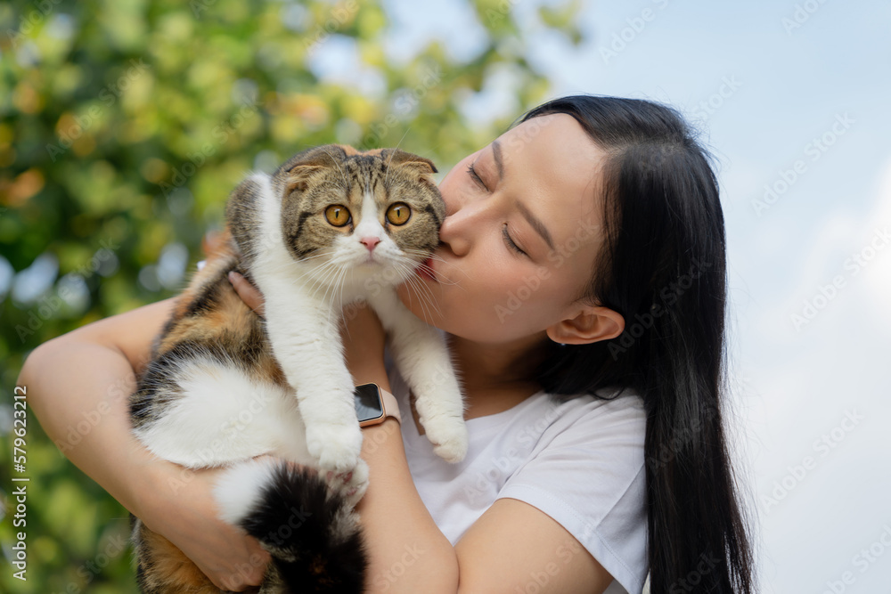 Beautiful young girl holds a Scottish cat with orange eyes, outdoor, close-up