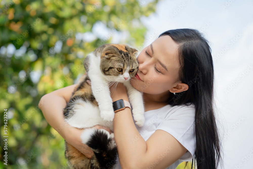 Asian woman with long black hair hugging her pet with a smile. She is playing with a cat. Pets and lifestyle concept.
