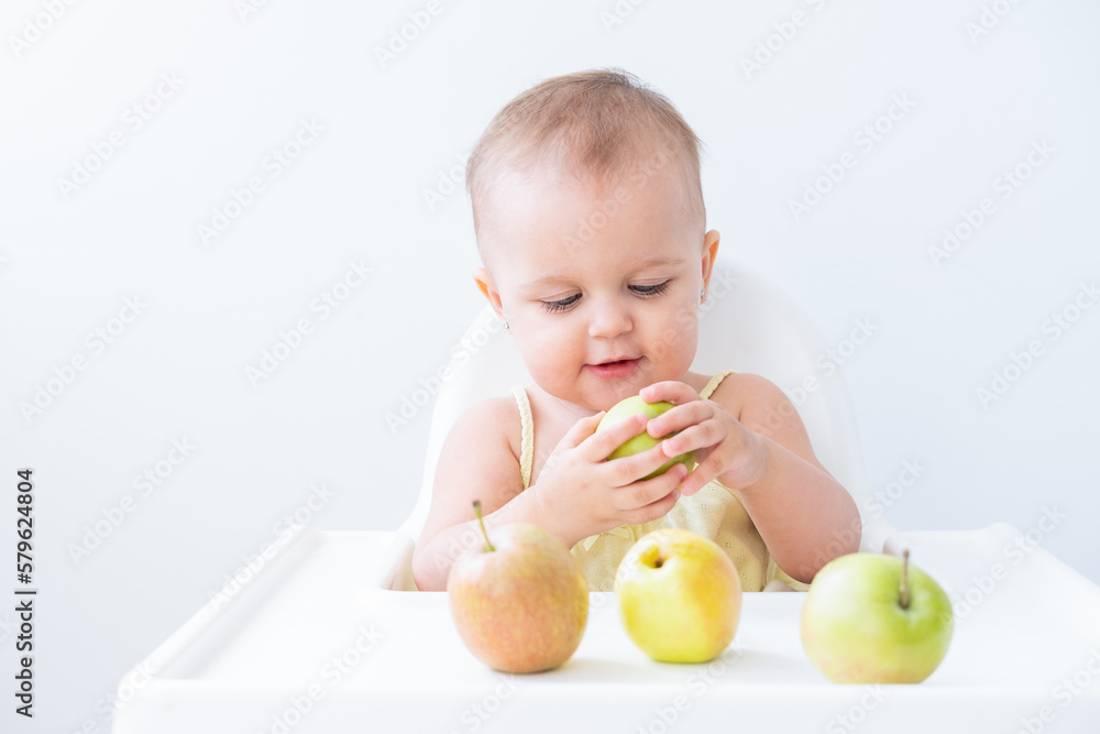 cute baby girl in baby chair eating apples. Baby first solid food cute baby girl in baby chair eating apples. Baby first solid food