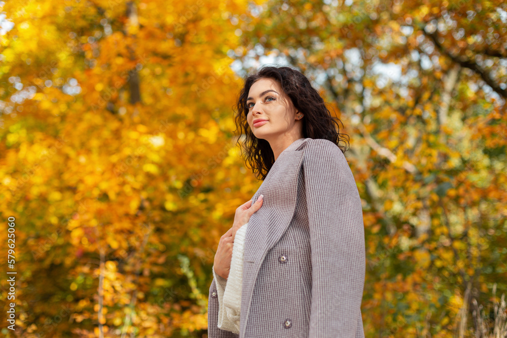 Beautiful curly autumn fashion woman in a stylish coat with a sweater walks in a golden autumn park Beautiful curly autumn fashion woman in a stylish coat with a sweater walks in a golden autumn park