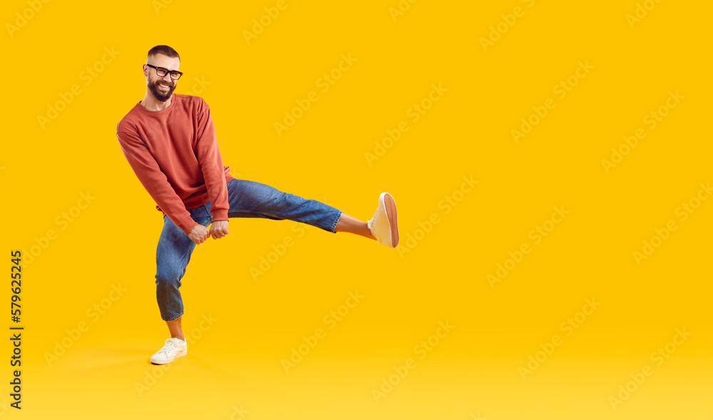 Funny young man in modern outfit dancing on copy space studio background. Happy guy in orange sweatshirt, blue jeans and glasses dancing isolated on yellow copyspace background. Casual fashion concept Funny young man in modern outfit dancing on copy space studio background. Happy guy in orange sweatshirt, blue jeans and glasses dancing isolated on yellow copyspace background. Casual fashion concept