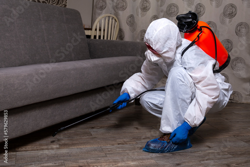 An exterminator in work clothes sprays pesticides with a spray gun. Fight against insects in apartments and houses. Disinsection of the premises