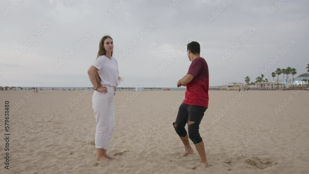 Young teen caucasian couple funny dancing on sand beach. Attractive girl and fit boy. Boyfriend and girlfriend enjoying spending time in love together. Date near sea. Palms on background. 4k Young teen caucasian couple funny dancing on sand beach. Attractive girl and fit boy. Boyfriend and girlfriend enjoying spending time in love together. Date near sea. Palms on background. 4k