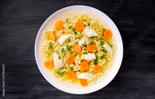 Homemade chicken soup with noodles and vegetables in a white bowl, on a black background.