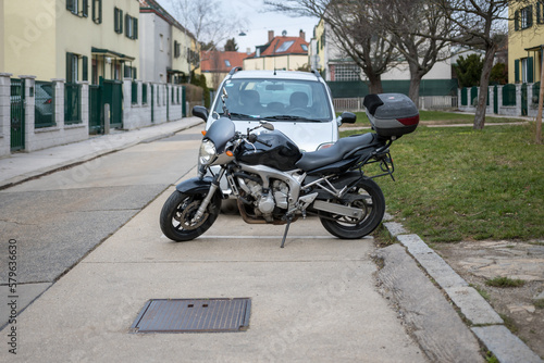Black motorcycle parking on a street in front of a car in the 10th district of Vienna, Austria