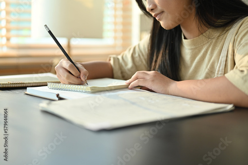 Focused asian girl writing task  doing homework while sitting at table in living room