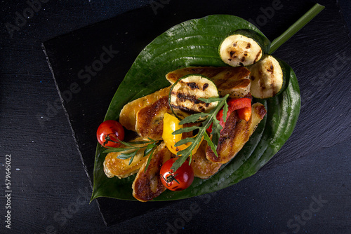 Overhead view of grilled halloumi cheese with cherry tomatoes, peppers and zucchini served in leaf on table photo