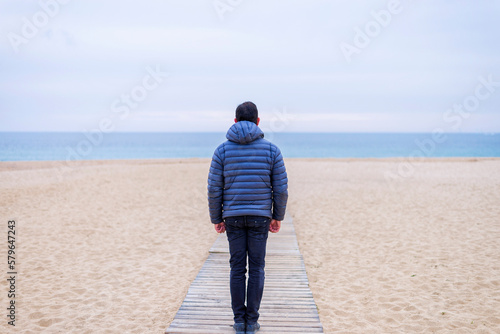 Rear view of man standing at beach contemplating the horizon photo