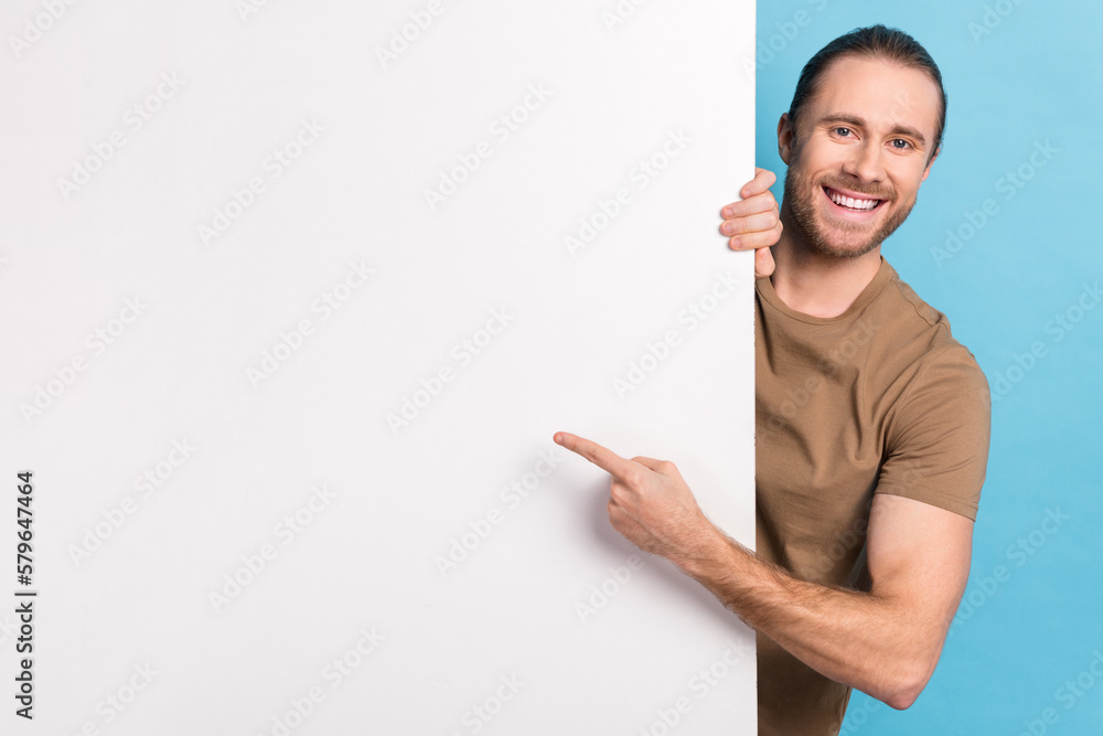Photo of cheerful positive guy dressed beige t-shirt pointing finger white placard emtpy space isolated blue color background Photo of cheerful positive guy dressed beige t-shirt pointing finger white placard emtpy space isolated blue color background