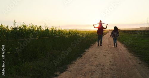 Family walking along a farm at sunset, bonding and having fun in nature. Agriculture, happy family and peaceful walk along a field of grass with parents and child talking, relaxing and enjoying view