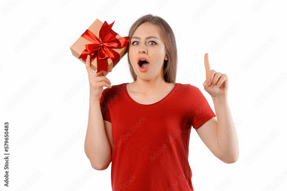 Portrait of a charming curious girl holding gift box at her ear and posing over white background. International Women's Day, New Year, Christmas, Birthday and Valentine's Day concept celebration Portrait of a charming curious girl holding gift box at her ear and posing over white background. International Women's Day, New Year, Christmas, Birthday and Valentine's Day concept celebration