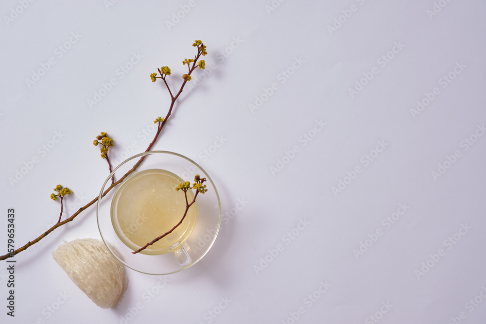 A glass transparent cup containing bird’s nest soup, decorated with an edible bird’s nest and flower branches. Bird’s nest can enhance disease prevention system. Blank space to display product