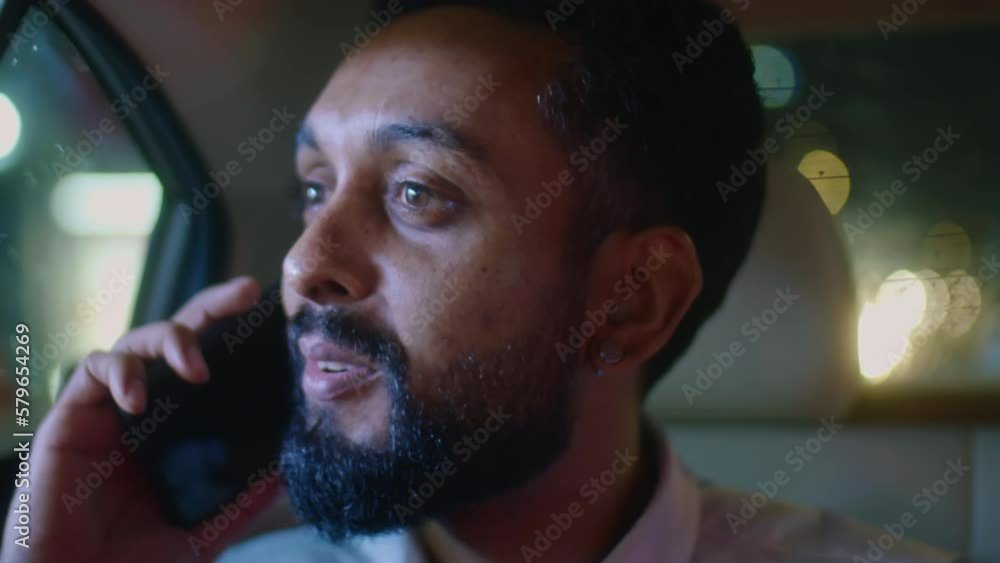 Close up shot of businessman speaking on mobile phone and looking at night city through car window while riding in backseat of taxi Close up shot of businessman speaking on mobile phone and looking at night city through car window while riding in backseat of taxi