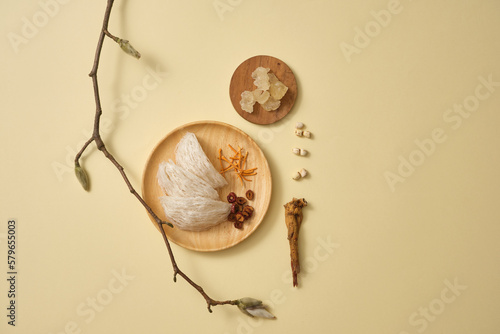 Edible bird’s nest placed on a wooden dish with herbs such as jujube, cordyceps, lotus seeds and ginseng. A dish of rock sugar beside. Healthy food for health, brain and bone photo