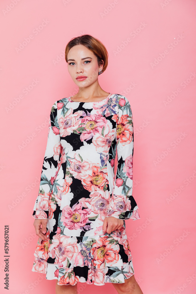 a woman in a floral dress stands against a pink wall a woman in a floral dress stands against a pink wall