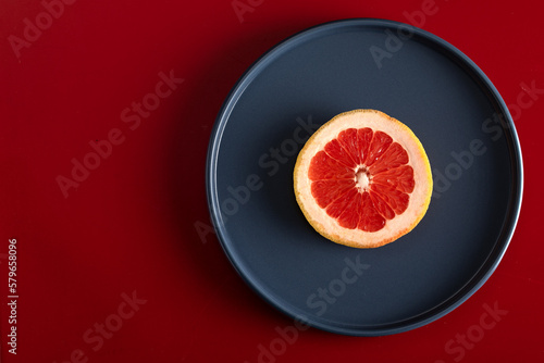 A slice of grapefruit on a blue plate. plate on a red background. View from above. Space for text.