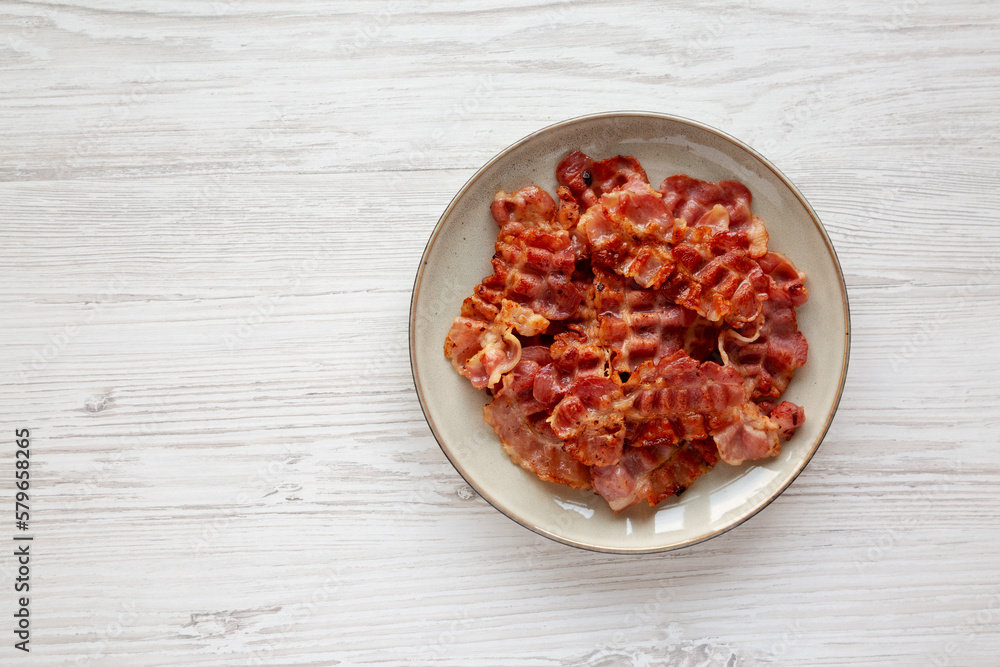 Cooked Greasy Bacon on a Plate on a white wooden background, top view. Space for text.