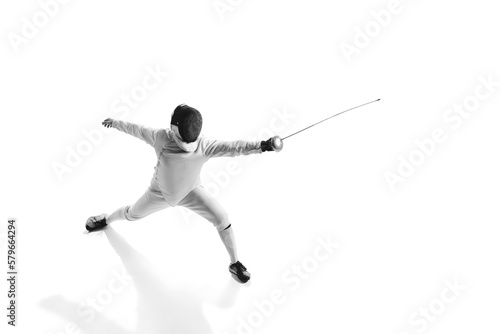 Dynamic portrait of male athlete in fencing costume with sword in hand in action isolated on white studio background. © Lustre Art Group 