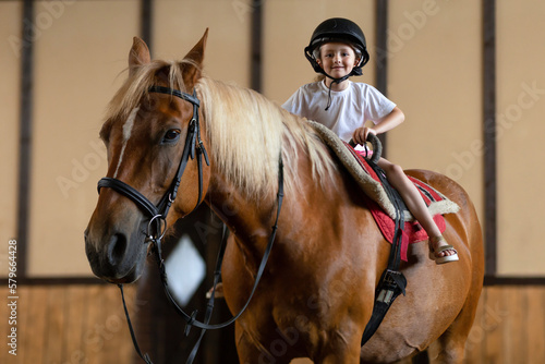 Smiling little girl in helmet learning horseback riding. .Happy child teaching equestrian on horse