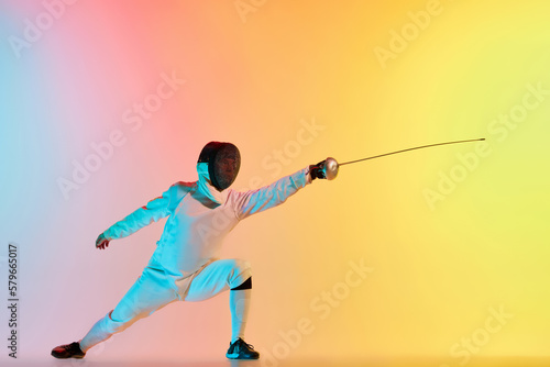 Long attack. Young man, male fencer with sword practicing in fencing over gradient pink-yellow background in neon light. Sportsman shows fencing technique