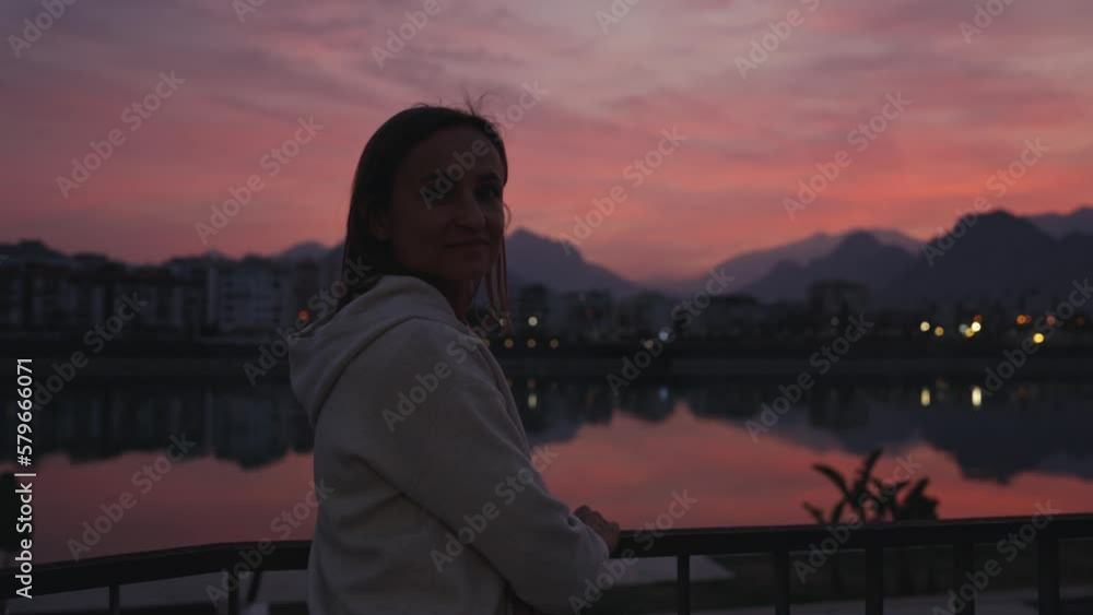 Rear View Of Woman enjoying beautiful pink sunset in city. Woman On River In City At Sunset. Rear View Of Woman enjoying beautiful pink sunset in city. Woman On River In City At Sunset.
