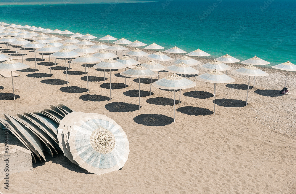 A row of beach umbrellas in blue color on the seashore with turquoise water.
