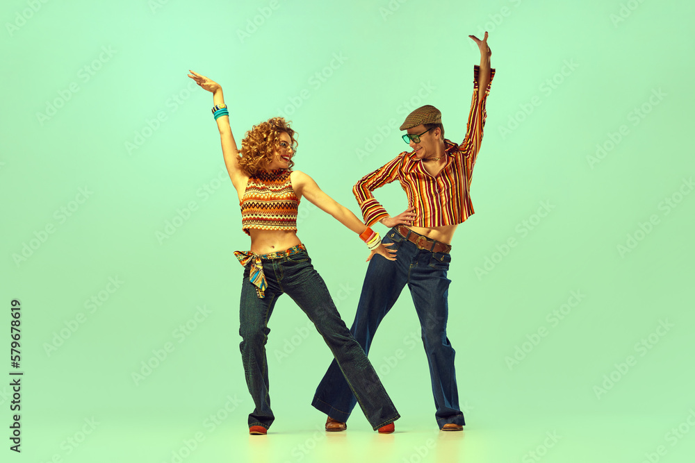 Fototapeta premium Incendiary dance. Emotional man and woman in retro style clothes dancing disco dance over green background. Concept of fashion trends of 70s, 1980s years, music