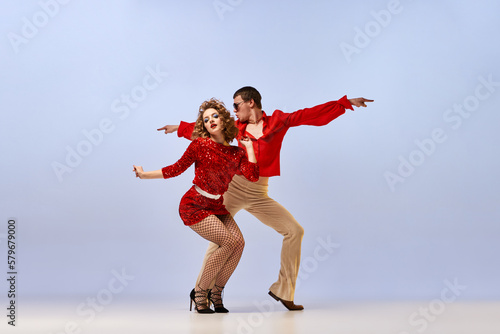 Young beautiful couple of dancers in bright retro fashion clothes, stage costumes dancing over lilac color background. Concept of music, art, dance, retro