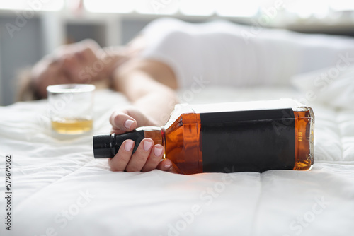 Bilde på lerret Woman lies in white bed with bottle of whiskey in hand