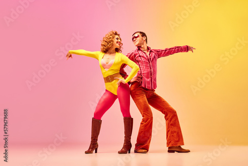 Disco dance. Stylish expressive excited couple of professional dancers in retro style clothes dancing over pink-yellow background.