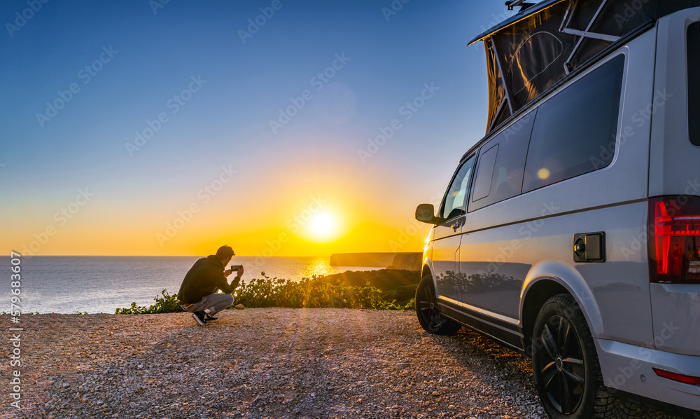man standing with digital device at his Transporter Camping Van bus at the California Ocean in the coastal Nature - digital nomad concept