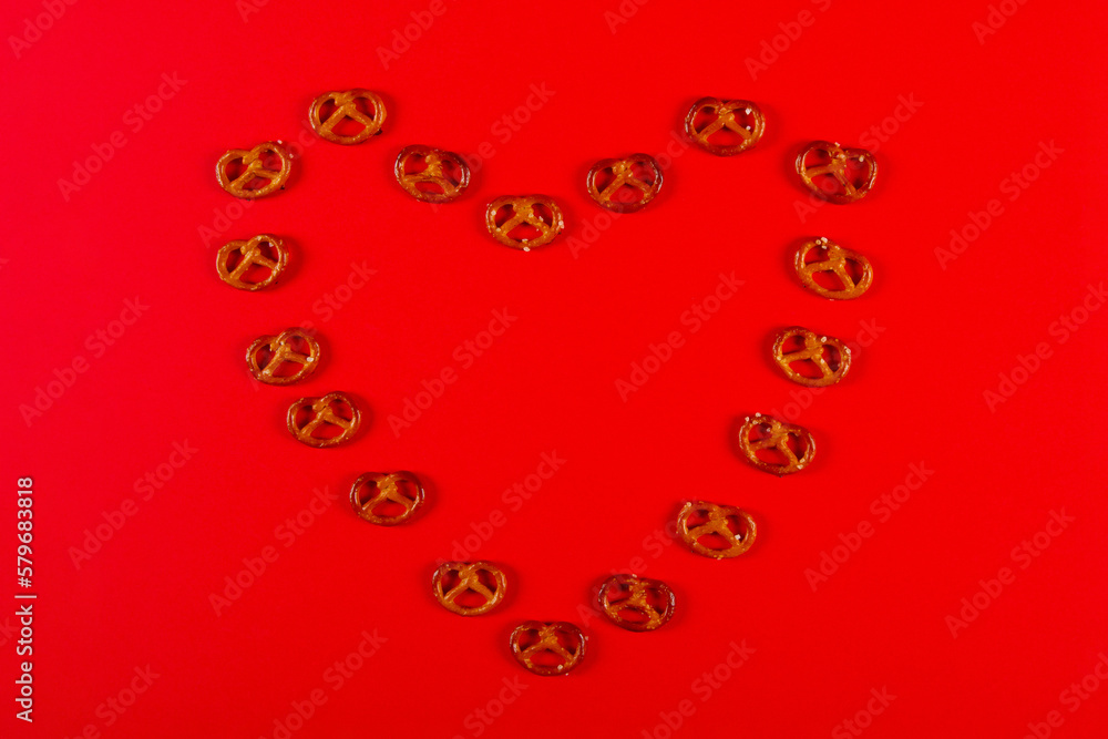 Mini pretzels in the shape of heart lie on vibrant red background. Pretzel Sunday concept