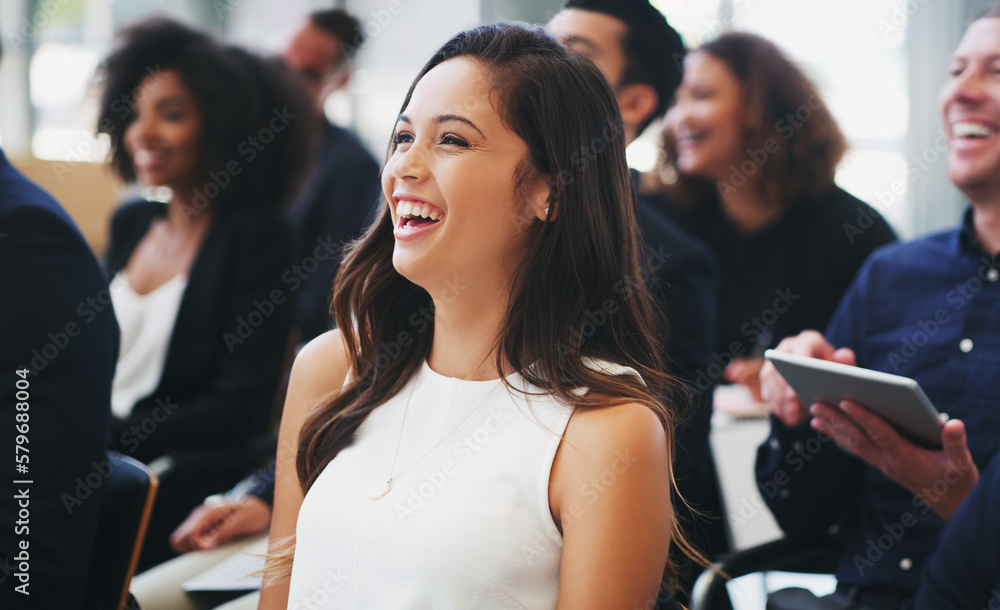 Opening the presentation with some in house humour. Shot of a happy young businesswoman sitting in the audience of a business conference.