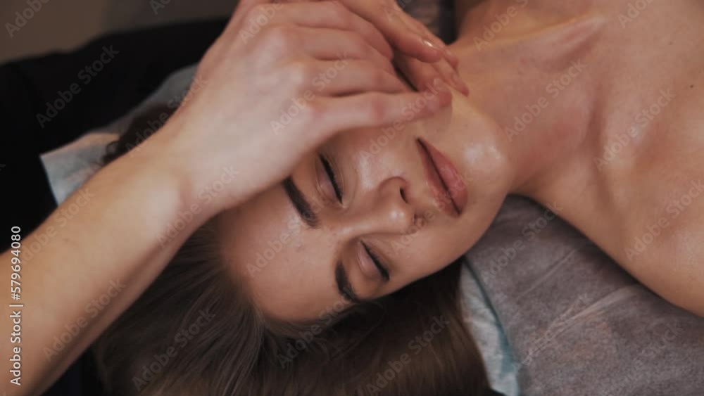Close-up portrait of a pretty woman receiving a gentle face massage of a young woman in a soft light massage room Close-up portrait of a pretty woman receiving a gentle face massage of a young woman in a soft light massage room