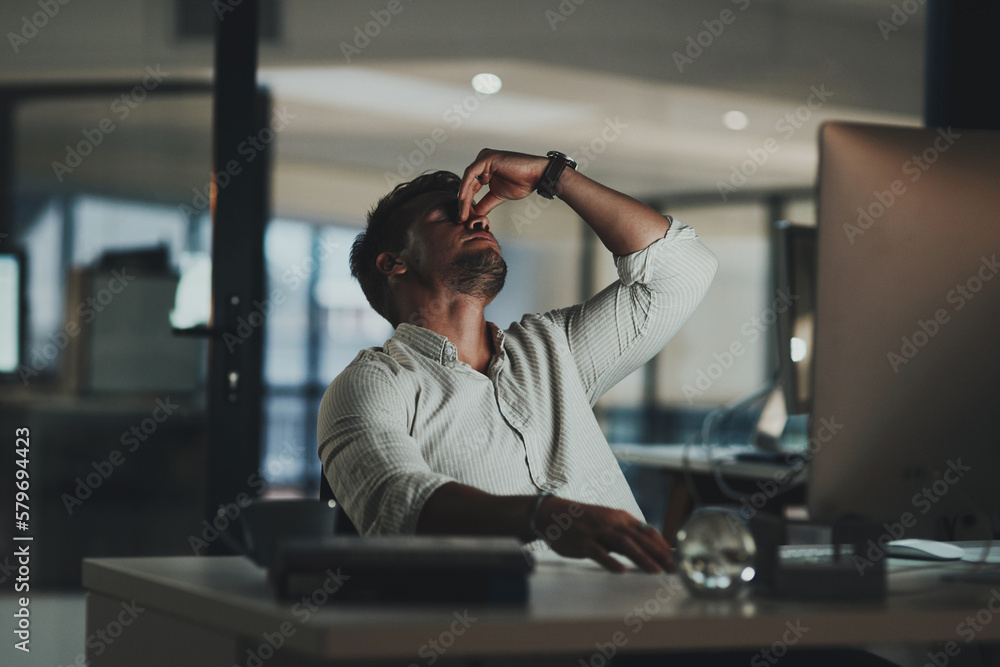 I just cant focus. Shot of a young businessman looking stressed out while working on a computer in an office at night. - obrazy, fototapety, plakaty 
