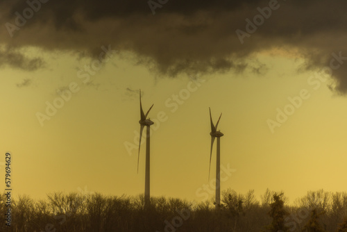 two windmills in a flat landscape with dark rainclouds and yellow color