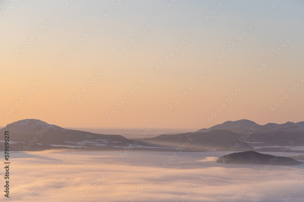 霞んだ夜明けの山々のシルエットと靄に覆われた湖。