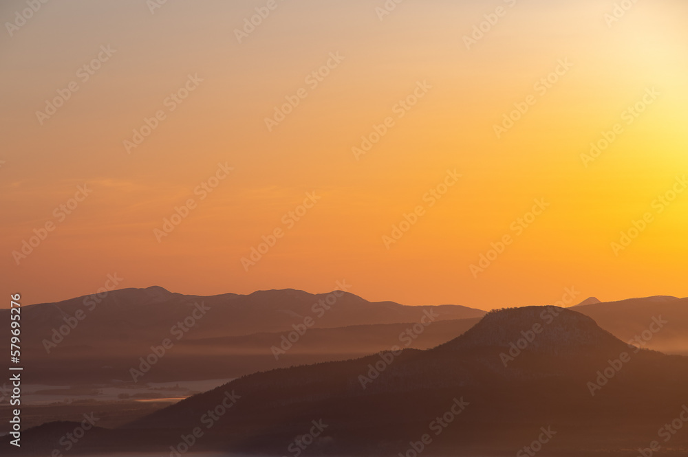 オレンジ色の夜明けの空と遠くの山々のシルエット。