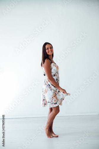 a woman in a floral dress poses on a white wall in a room