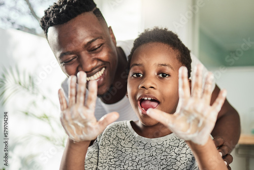 Good hygiene habits will keep you healthy. Portrait of a boy holding up his soapy hands while standing in a bathroom with his father at home.