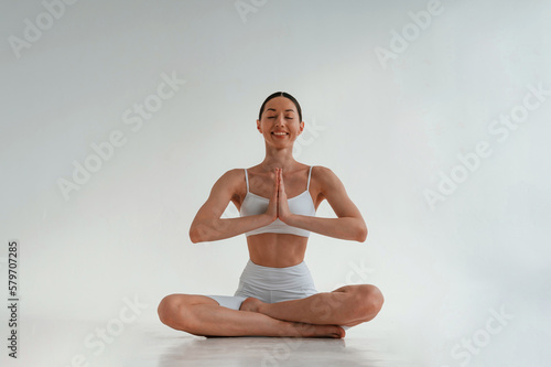 Sitting in a lotus pose. Young caucasian woman with slim body shape is indoors in the studio