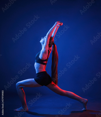 Doing sportive exerises. Beautiful muscular woman is indoors in the studio with neon lighting