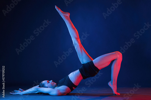 View from the side, lying down on the floor. Beautiful muscular woman is indoors in the studio with neon lighting